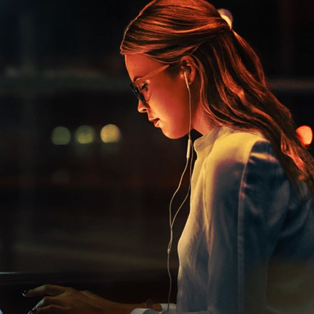 Young woman working late at night on her laptop while wearing earphones.