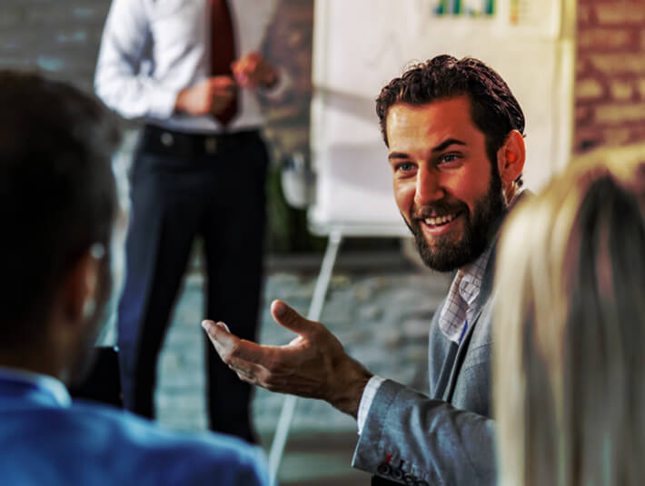 Young happy businessman turning to his colleague and talking to him during a presentation in a board room.